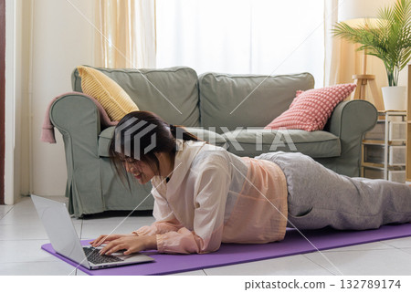 Healthy lifestyle woman teen maintains physical health, engaging in exercise workout at home, happily practicing yoga pose on mat, utilizing laptop for virtual sport training, promoting wellbeing. Healthy lifestyle woman teen maintains physical health, engaging in exercise workout at home, happily practicing yoga pose on mat, utilizing laptop for virtual sport training, promoting wellbeing. 132789174