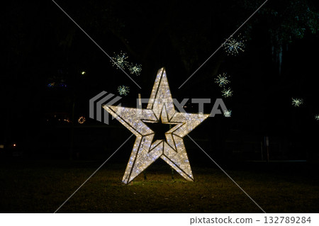 A large glowing star stands on a dark lawn with twinkling lights behind it. The holiday display creates a festive winter scene in the downtown park. 132789284