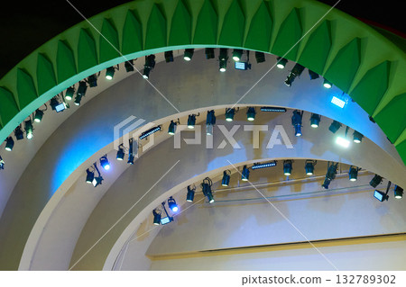 Rows of professional stage lights hang beneath curved green arches. Bright LEDs illuminate a concert venue for a live event at night. Rows of professional stage lights hang beneath curved green arches. Bright LEDs illuminate a concert venue for a live event at night. 132789302