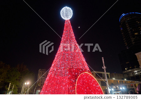 A tall red LED Christmas tree shines brightly against the dark sky in the city. Festive holiday lights create a cheerful downtown winter celebration. 132789305