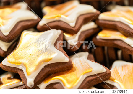 Captured from a macro perspective, a stack of golden star-shaped cookies with a rich chocolate base is elegantly decorated with white royal icing and shimmering gold accents. The intricate detailing 132789443
