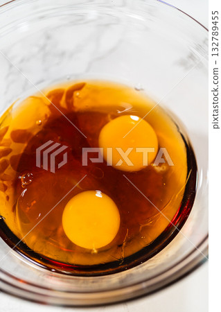 Close-up top view of a glass bowl containing two raw eggs and maple syrup, forming a dark base mixture for the Amber Gingerbread Cookie Dough. Close-up top view of a glass bowl containing two raw eggs and maple syrup, forming a dark base mixture for the Amber Gingerbread Cookie Dough. 132789455