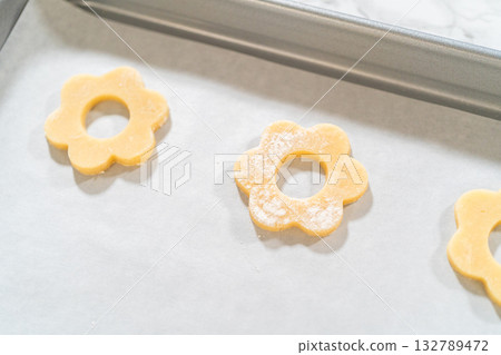 Cut-out flower cookies with holes in the center on parchment-lined baking sheet, pre-bake step for Easter Cookie Sandwich with Raspberry Buttercream. 132789472