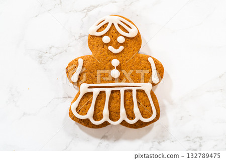 A single decorated gingerbread girl cookie on a marble countertop, showcasing its intricate royal icing dress and smiling face. 132789475