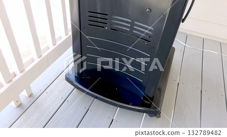A vertical outdoor barbecue grill with a black and silver finish stands on a light-colored wooden deck. The bottom panel and curved design are clearly visible. A vertical outdoor barbecue grill with a black and silver finish stands on a light-colored wooden deck. The bottom panel and curved design are clearly visible. 132789482