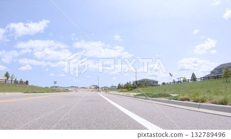 A road in Castle Rock, Colorado gently curves ahead with a landscaped center divider and residential homes along both sides. The street appears newly constructed. 132789496