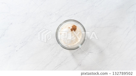 Flat lay. Mixing dry ingredients with a hand whisk in a glass mixing bowl to prepare eggnog pancakes. Flat lay. Mixing dry ingredients with a hand whisk in a glass mixing bowl to prepare eggnog pancakes. 132789502