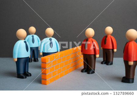 A brick wall separates two ideological camps of office workers. Two opposing teams or business departments. Competition, team disagreement, or workplace polarization. A brick wall separates two ideological camps of office workers. Two opposing teams or business departments. Competition, team disagreement, or workplace polarization. 132789660