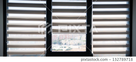 Three modern windows with zebra roller blinds filtering daylight in minimalist apartment 132789718