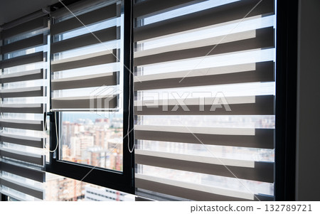 Zebra roller blinds partially open on modern apartment windows with cityscape view Zebra roller blinds partially open on modern apartment windows with cityscape view 132789721