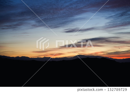Sunset landscape with colorful sky and mountains in silhouette under evening light and clouds 132789729