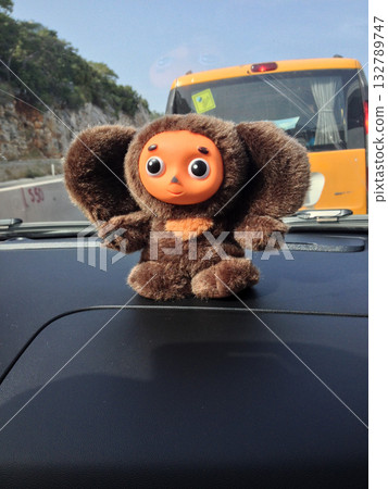 Plush toy Cheburashka sitting on car dashboard during road trip. Travel, nostalgia, and the playful charm of childhood memories on the road. Plush toy Cheburashka sitting on car dashboard during road trip. Travel, nostalgia, and the playful charm of childhood memories on the road. 132789747