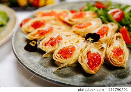 Festive crepe rolls with red caviar, greens and cherry tomatoes on elegant table setting 132790791