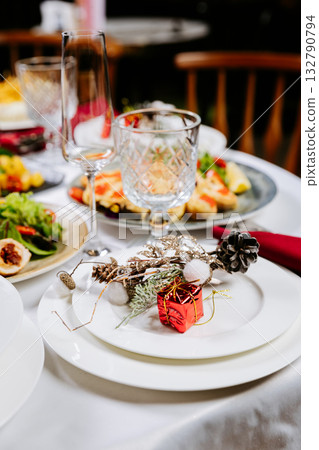 Elegant festive table setting with Christmas decor, white plates, and red gift accent 132790794