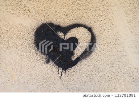 Black heart graffiti with dripping spray paint on textured beige wall, creating a raw street art aesthetic. Emotional background, rebellious urban expression, underground street art 132791091