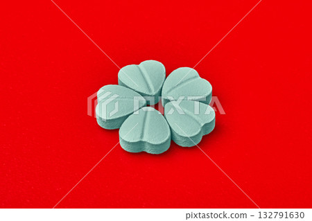Blue heart pills on a red background are arranged in the shape of a flower. Blue heart pills on a red background are arranged in the shape of a flower. 132791630