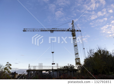 Construction cranes work on creation site against blue sky background. Construction cranes work on creation site against blue sky background. 132791651