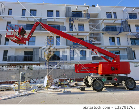 Construction site shows a self propelled articulated boom lift positioned near a building being constructed. Work is ongoing with materials scattered around. 132791765