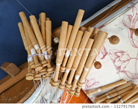 Wooden bobbins for hand weaving Valencian lace are neatly arranged on a patterned table. The lace-making activity shows a rich tradition and skill unique to the region. Wooden bobbins for hand weaving Valencian lace are neatly arranged on a patterned table. The lace-making activity shows a rich tradition and skill unique to the region. 132791769