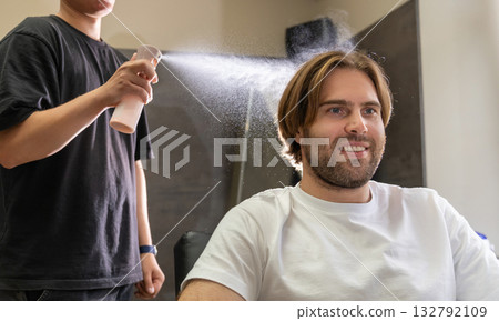 A barber sprays water on a male client's hair before a haircut. 132792109
