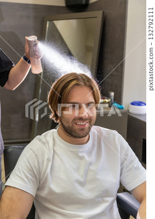 A barber sprays water on a male client's hair before a haircut. A barber sprays water on a male client's hair before a haircut. 132792111