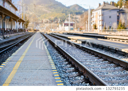 Empty train station in small city on sunny day, shallow depth of field photo, focus on concrete platform and steel rail foreground Empty train station in small city on sunny day, shallow depth of field photo, focus on concrete platform and steel rail foreground 132793235