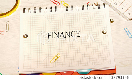 A spiral notebook with the word Finance written on the grid paper is seen on a desk with a calculator and colorful paper clips, representing financial planning 132793396