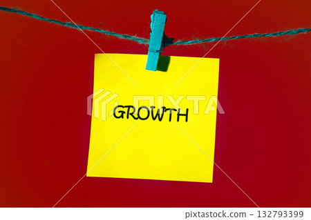 A yellow sticky note displaying the word GROWTH hangs from a teal string with a blue clip against a bold red backdrop, serving as a visual cue for success 132793399
