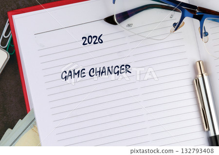 Open notebook displays the year 2026 and the phrase GAME CHANGER, accompanied by glasses and a pen, suggesting upcoming plans on a desk surface Open notebook displays the year 2026 and the phrase GAME CHANGER, accompanied by glasses and a pen, suggesting upcoming plans on a desk surface 132793408