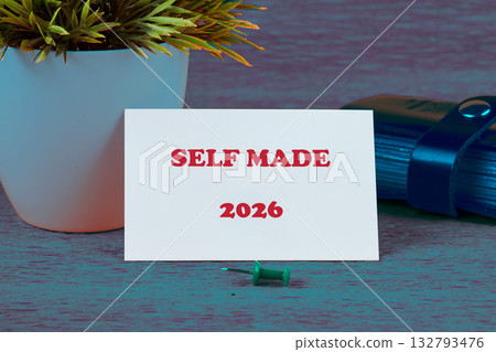 A small potted plant sits beside a card that reads Self Made 2026. A green pin and a blue roll are also on the surface, hinting at future achievements 132793476