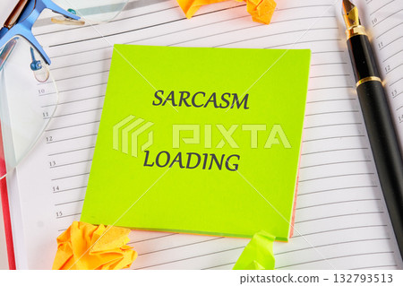 A bright green note with Sarcasm Loading is displayed on a planner next to a fountain pen, eyeglasses, and origami shapes. Be prepared for some sharp humor 132793513