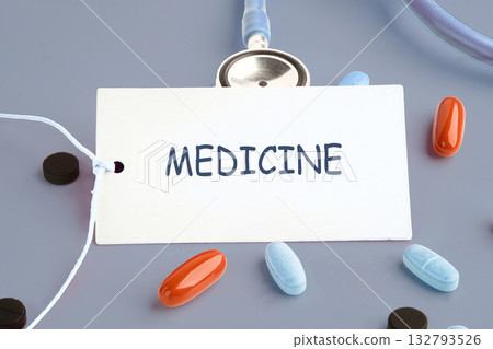 Pills of various sizes and colors sit near a card with the word MEDICINE written on it. A stethoscope is present, suggesting healthcare or a medical theme Pills of various sizes and colors sit near a card with the word MEDICINE written on it. A stethoscope is present, suggesting healthcare or a medical theme 132793526