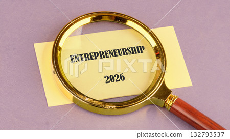 A magnifying glass focuses on a note that reads ENTREPRENEURSHIP 2026. This highlights examination of future business developments and new ventures in business development 132793537