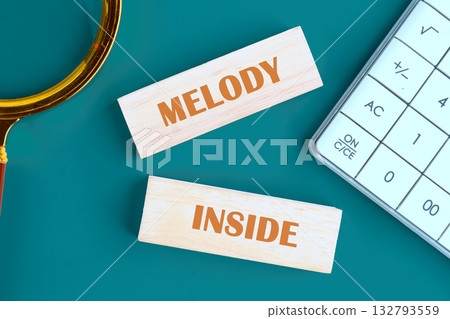 A magnifying glass, blocks spelling Melody Inside, and a calculator sit on a teal surface. The scene suggests uncovering hidden beauty through careful calculation and attention to detail A magnifying glass, blocks spelling Melody Inside, and a calculator sit on a teal surface. The scene suggests uncovering hidden beauty through careful calculation and attention to detail 132793559