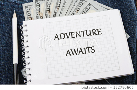 A notebook with the words ADVENTURE AWAITS rests on denim, accompanied by a pencil and some cash, suggesting a dream vacation is on the horizon 132793605