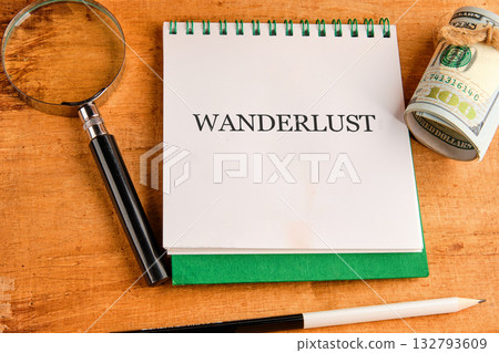A notebook with the word Wanderlust written on it rests near a magnifying glass, a roll of cash, and a pencil on a wooden table, suggesting plans for a big trip A notebook with the word Wanderlust written on it rests near a magnifying glass, a roll of cash, and a pencil on a wooden table, suggesting plans for a big trip 132793609