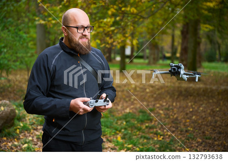 A man controls a small drone in a serene park filled with vibrant autumn leaves. The moment captures the joy of technology blending with nature's beauty. A man controls a small drone in a serene park filled with vibrant autumn leaves. The moment captures the joy of technology blending with nature's beauty. 132793638
