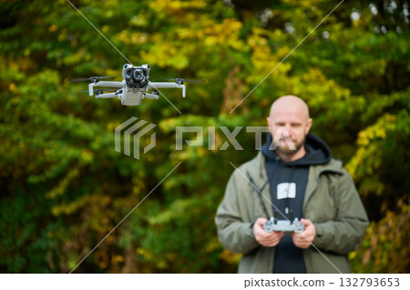 A man control a sleek drone in a lush area filled with colorful autumn trees, showcasing his skills and passion for technology in nature's beauty. 132793653