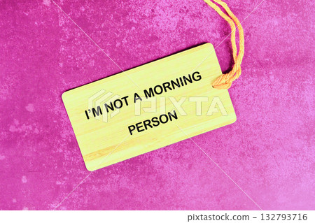 A light yellow tag rests on a textured, bright pink surface. The tag declares, Im NOT A MORNING PERSON in bold, black capital letters. Its attached with a yellow string A light yellow tag rests on a textured, bright pink surface. The tag declares, Im NOT A MORNING PERSON in bold, black capital letters. Its attached with a yellow string 132793716
