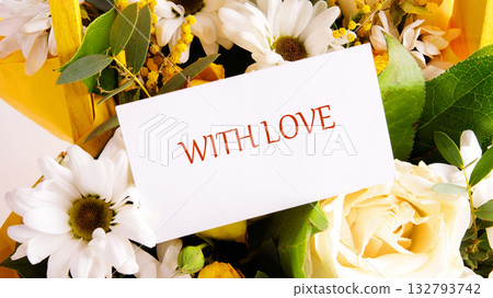 A close-up shows a lovely gift of daisies and roses. A card nestled among the blooms says WITH LOVE in red letters. The present arrives with sunshine and smiles 132793742