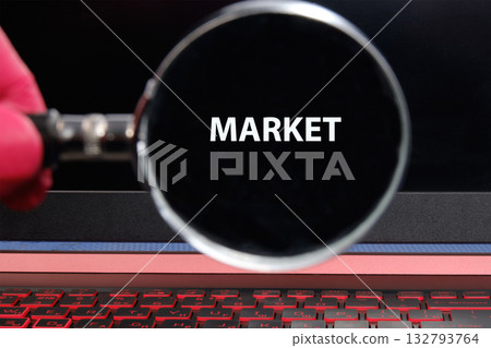 A hand holds a magnifying glass over a laptop screen displaying the word market. This scene captures the essence of searching and analyzing online business opportunities 132793764