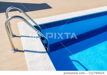 Closeup of pool ladder and tiles. sunlit blue water, stainless steel ladder, concrete deck, crisp geometric lines, inviting entry for swimmers, summer staycation Closeup of pool ladder and tiles. sunlit blue water, stainless steel ladder, concrete deck, crisp geometric lines, inviting entry for swimmers, summer staycation 132794024
