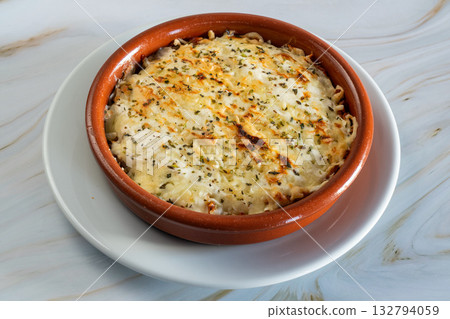 Creamy Kapsalon baked macaroni and cheese resting in ceramic ramekin with golden crust, sprinkled parsley, set on white plate over marble counter, warm homestyle comfort meal 132794059