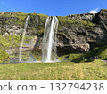 This is a picture of Seljalandsfoss, a waterfall in southern Iceland, seen from the front, with a rainbow and blue sky. 132794238