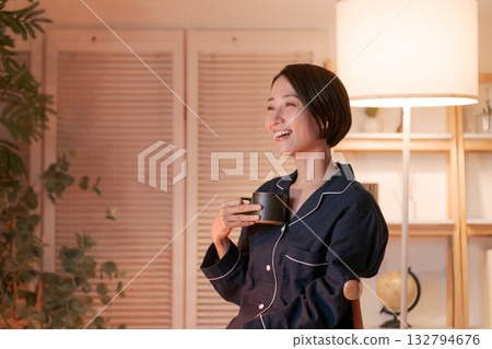 Woman in pajamas drinking a hot drink in her room at night Woman in pajamas drinking a hot drink in her room at night 132794676