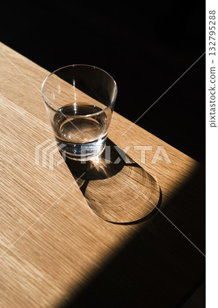 Glass of water casting shadow on wooden table Glass of water casting shadow on wooden table 132795288