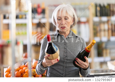 Shopping in produce supermarket - mature female buyer makes choice bottle of wine Shopping in produce supermarket - mature female buyer makes choice bottle of wine 132795907