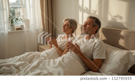 Couple practicing deep breathing exercises in a cozy bedroom, surrounded by soft lighting and serene atmosphere, promoting relaxation before sleep 132795935