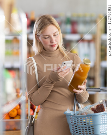 Girl scan QR code, take reading peach juice label using phone camera in shop 132795985