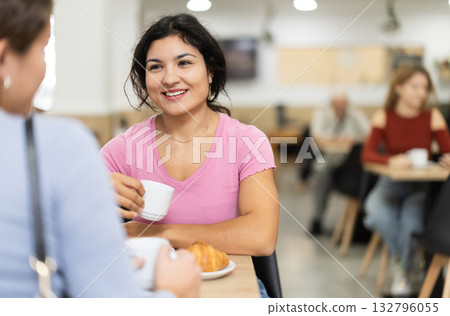 Young girl chatting with friend over coffee and croissant in cafeteria 132796055